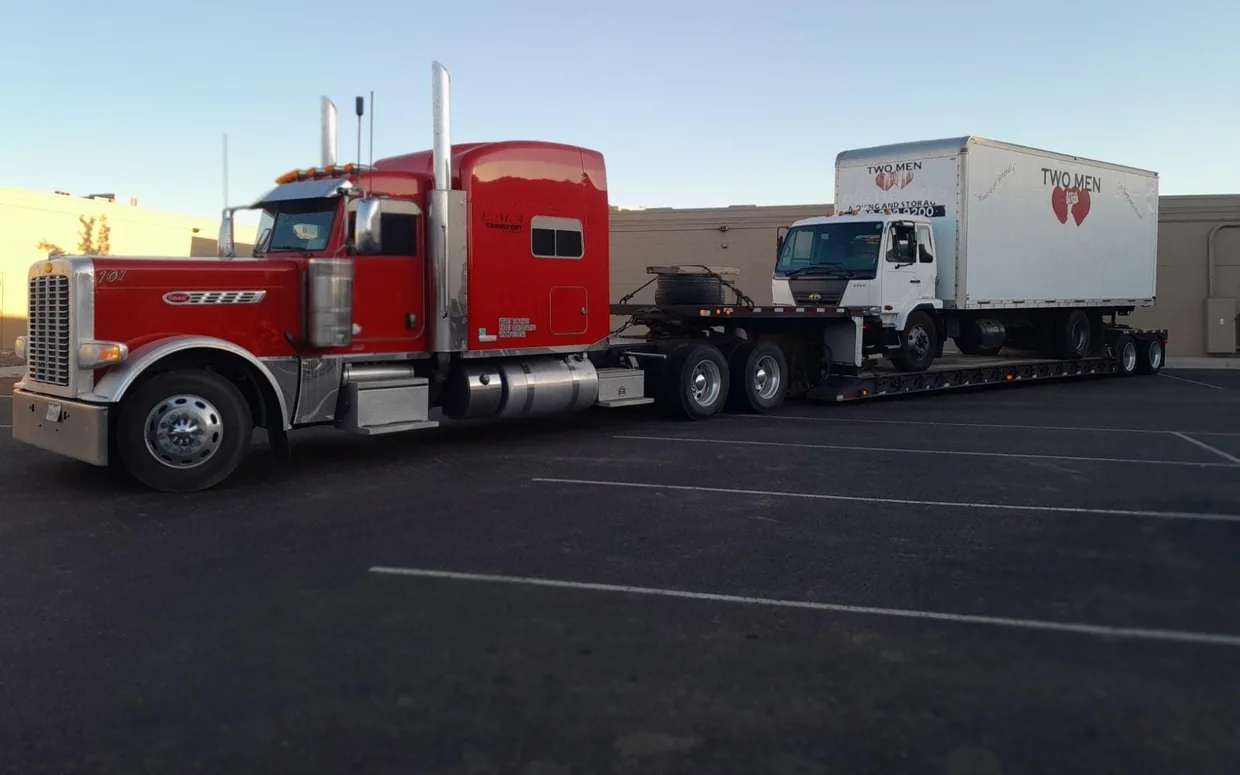 Red semi-truck hauling a box truck on a step-deck trailer